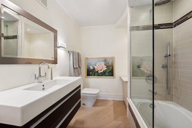 bathroom with baseboards, toilet, wood finished floors, enclosed tub / shower combo, and vanity