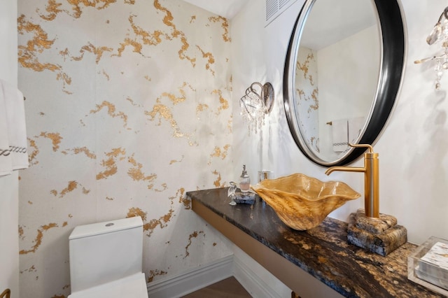 bathroom with wallpapered walls, toilet, and a sink