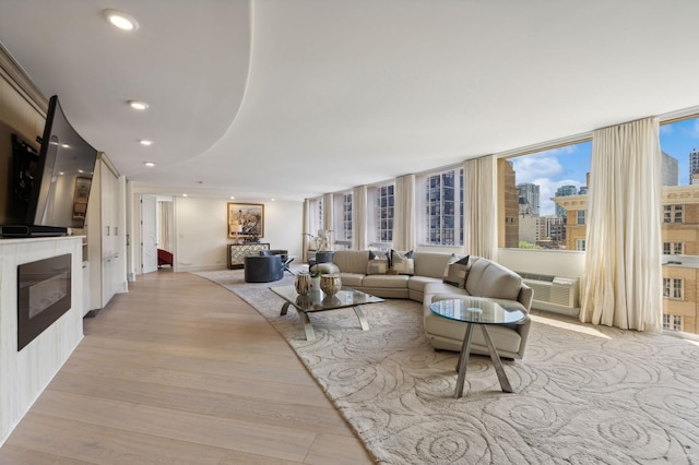 living area with recessed lighting, light wood-style floors, a glass covered fireplace, and a wall mounted air conditioner