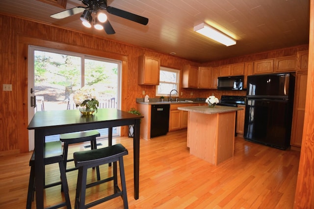 kitchen featuring wooden walls, a sink, light wood-style floors, black appliances, and a center island