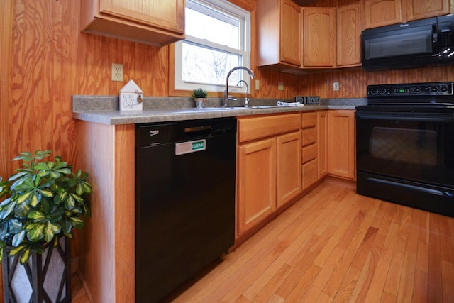 kitchen with light countertops, a sink, light wood-style floors, wooden walls, and black appliances
