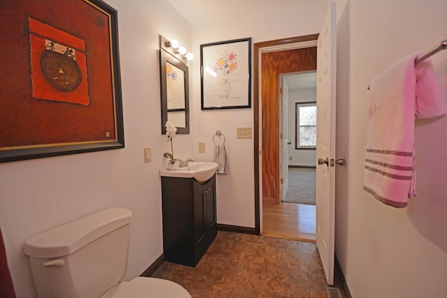 half bathroom with toilet, vanity, stone finish floor, baseboards, and visible vents
