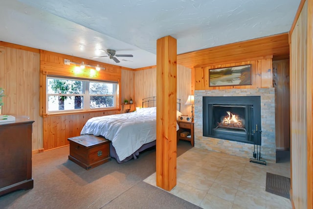 bedroom featuring a ceiling fan, wood walls, and a lit fireplace