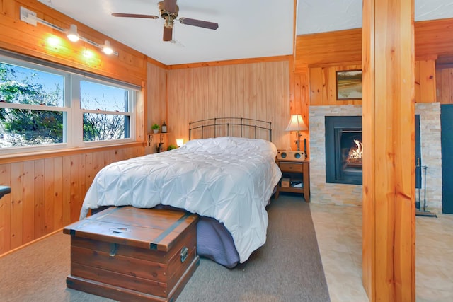 bedroom featuring a warm lit fireplace, wood walls, and a ceiling fan