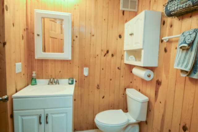 half bathroom featuring visible vents, wooden walls, toilet, and vanity