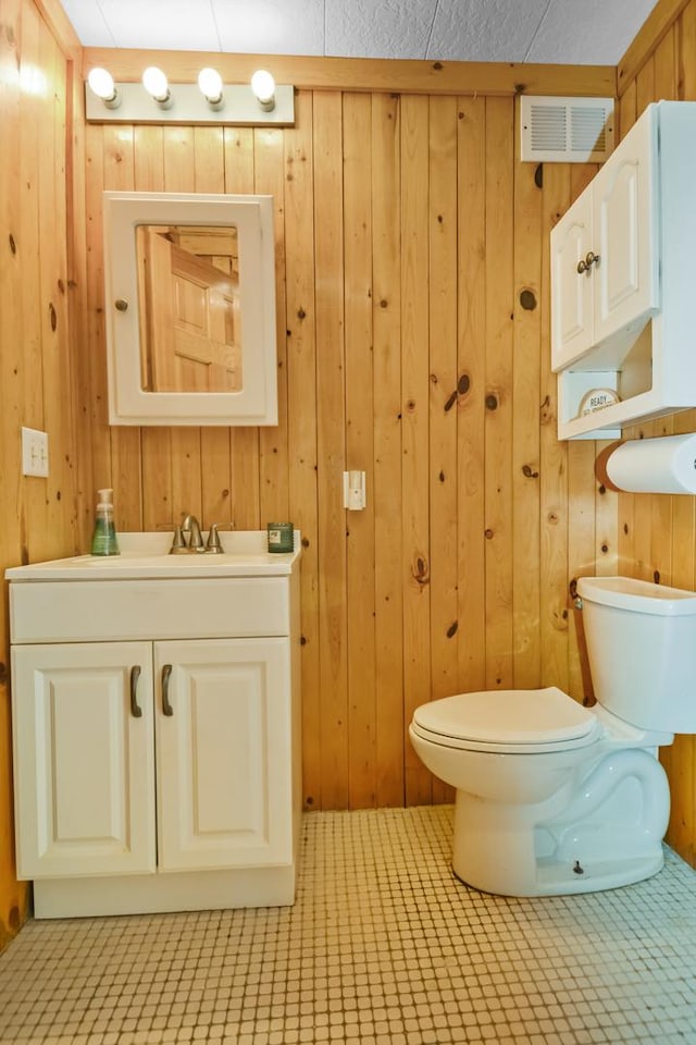 half bath with visible vents, wooden walls, toilet, and vanity
