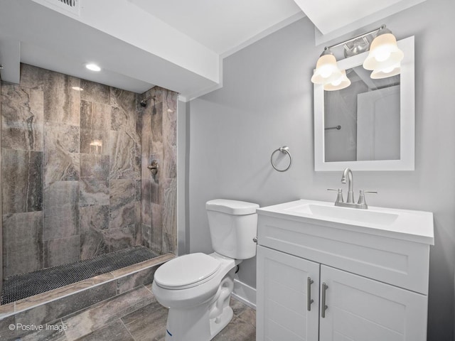 bathroom with vanity, toilet, baseboards, and tiled shower