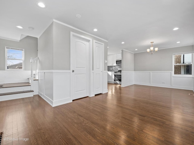 unfurnished living room with wainscoting, dark wood-style flooring, a wealth of natural light, and a chandelier