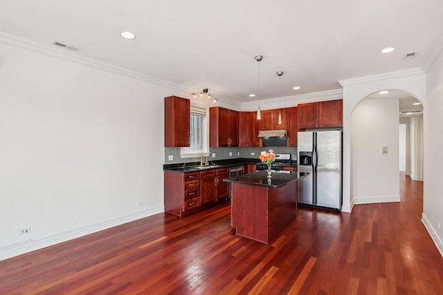 kitchen with dark countertops, under cabinet range hood, arched walkways, stainless steel appliances, and a sink