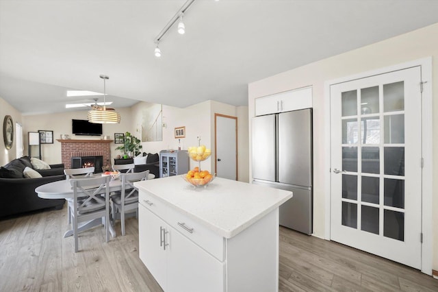 kitchen featuring stainless steel refrigerator, a fireplace, light wood-type flooring, and a kitchen island