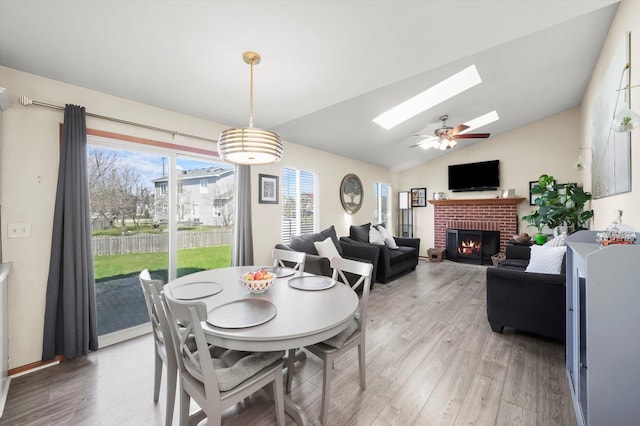 dining room featuring vaulted ceiling with skylight, light wood-style flooring, and a brick fireplace