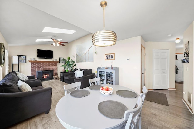 dining area featuring light wood-style flooring, ceiling fan, lofted ceiling with skylight, and a fireplace