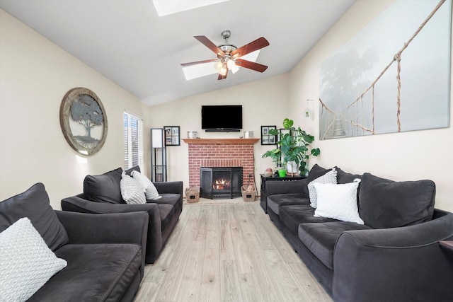 living area featuring a fireplace, vaulted ceiling with skylight, light wood-type flooring, and a ceiling fan