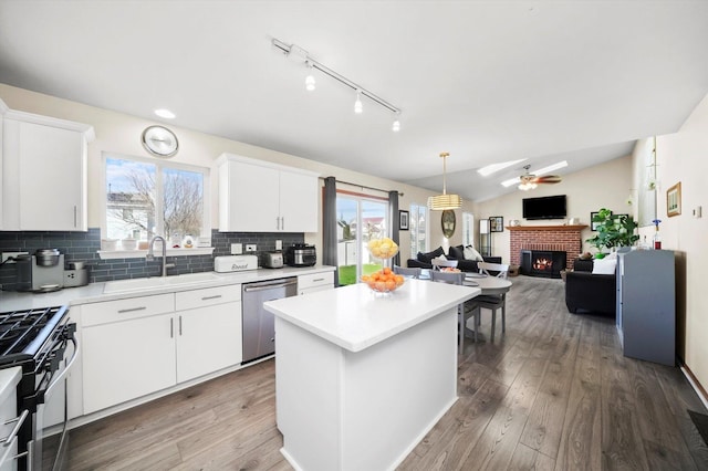 kitchen featuring gas range oven, a fireplace, a ceiling fan, stainless steel dishwasher, and a sink
