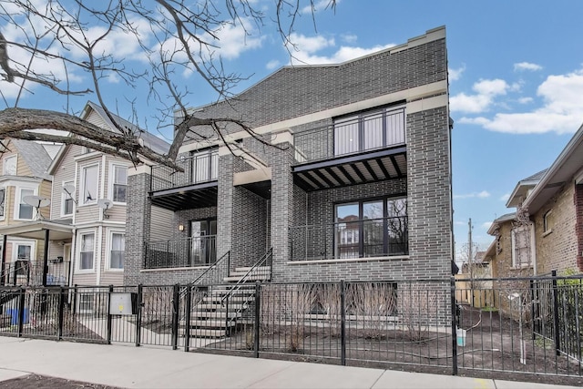 view of front of property with covered porch, brick siding, a balcony, and a fenced front yard