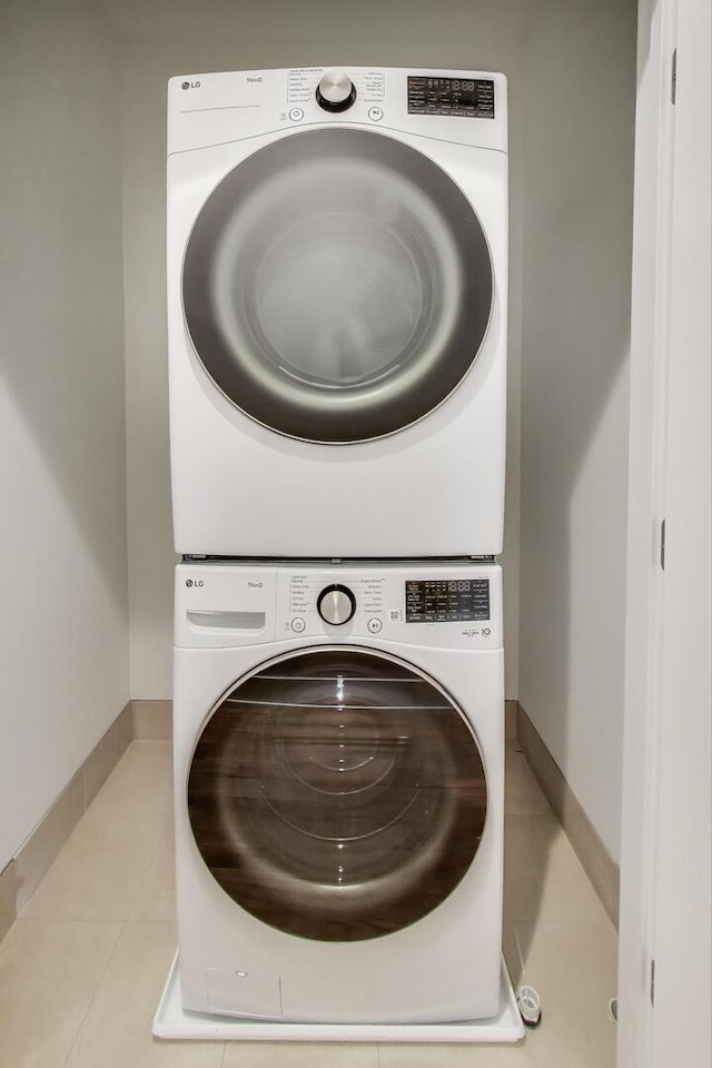 clothes washing area featuring stacked washer and dryer, baseboards, tile patterned flooring, and laundry area