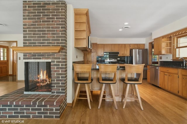 kitchen featuring open shelves, a fireplace, stainless steel appliances, light wood-style floors, and under cabinet range hood
