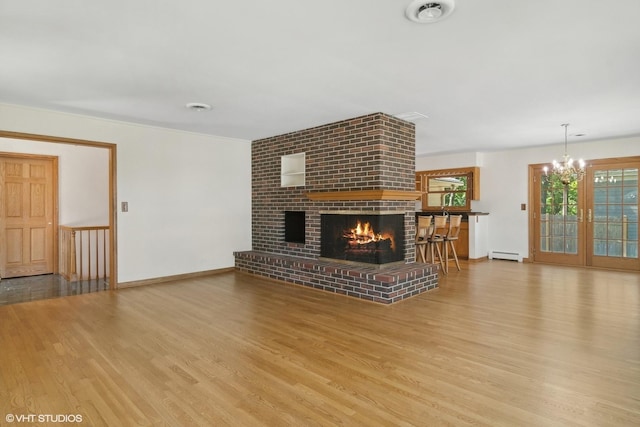 unfurnished living room featuring wood finished floors, baseboards, a brick fireplace, a notable chandelier, and baseboard heating