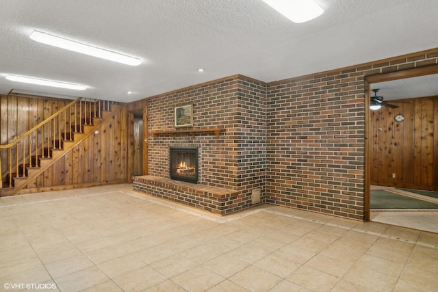 unfurnished living room with stairway, wood walls, a fireplace, and a textured ceiling