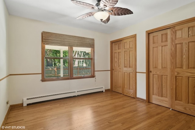 unfurnished bedroom featuring baseboards, ceiling fan, light wood-style floors, a baseboard heating unit, and two closets