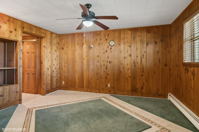 unfurnished room featuring light tile patterned floors, baseboard heating, wood walls, and a ceiling fan