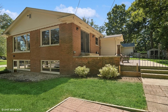 view of property exterior featuring brick siding, a lawn, an outbuilding, and fence