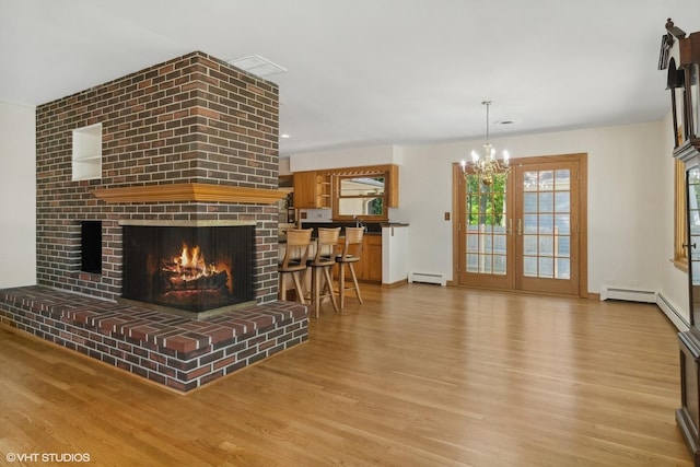 living area featuring an inviting chandelier, a brick fireplace, wood finished floors, and a baseboard radiator