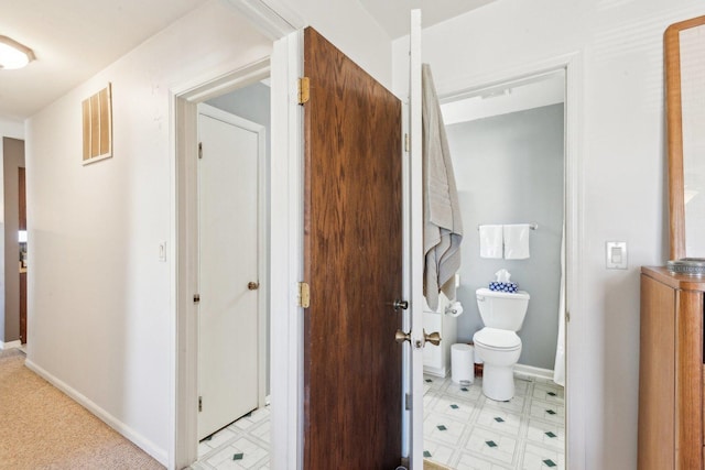 hall featuring visible vents, baseboards, and light floors