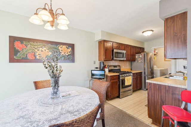 kitchen with a chandelier, decorative backsplash, appliances with stainless steel finishes, washer and dryer, and a sink