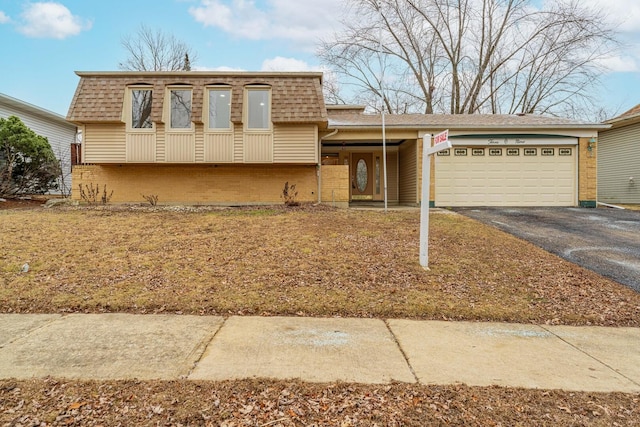 view of front of home with an attached garage, brick siding, driveway, and mansard roof