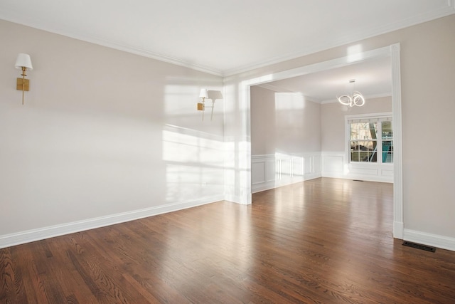 spare room featuring an inviting chandelier, crown molding, wood finished floors, and a wainscoted wall