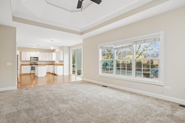 unfurnished living room featuring visible vents, a tray ceiling, ornamental molding, light carpet, and a ceiling fan
