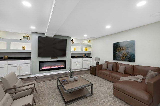 living room with recessed lighting, a glass covered fireplace, wood finished floors, and built in shelves