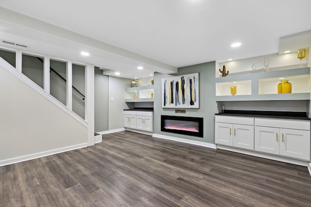 unfurnished living room with recessed lighting, baseboards, a glass covered fireplace, and dark wood-type flooring