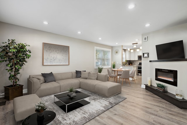 living area with a glass covered fireplace, light wood-style floors, recessed lighting, and visible vents