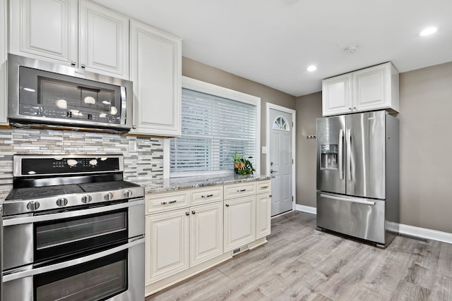 kitchen featuring decorative backsplash, light stone countertops, light wood-type flooring, baseboards, and stainless steel appliances