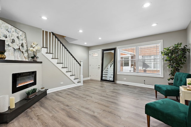entryway with recessed lighting, a glass covered fireplace, wood finished floors, and stairway