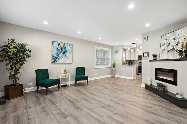 sitting room featuring recessed lighting, baseboards, a glass covered fireplace, and light wood finished floors