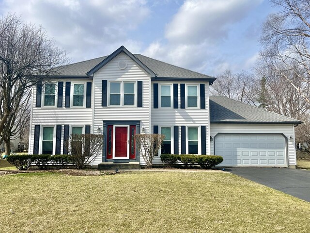 colonial house with driveway, a front lawn, an attached garage, and a shingled roof