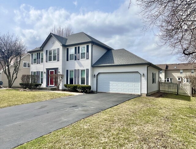 colonial home with an attached garage, driveway, a front yard, and fence