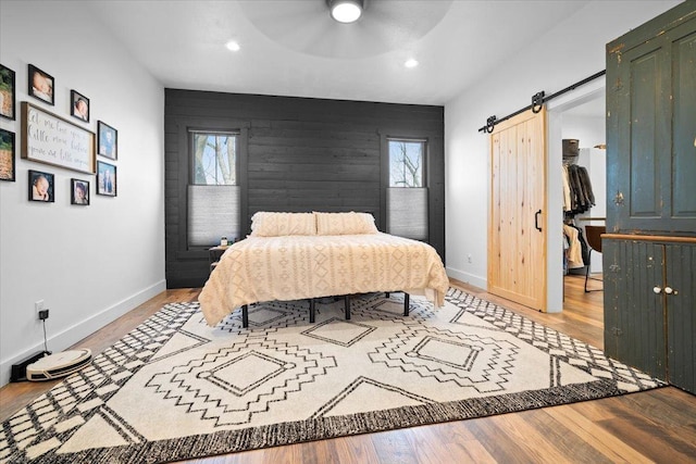 bedroom featuring multiple windows, a barn door, baseboards, wood finished floors, and recessed lighting