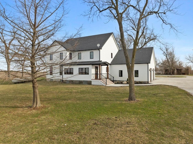 rear view of property with concrete driveway, a lawn, and a shingled roof