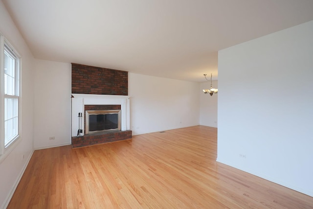 unfurnished living room featuring light wood finished floors, plenty of natural light, an inviting chandelier, and a fireplace