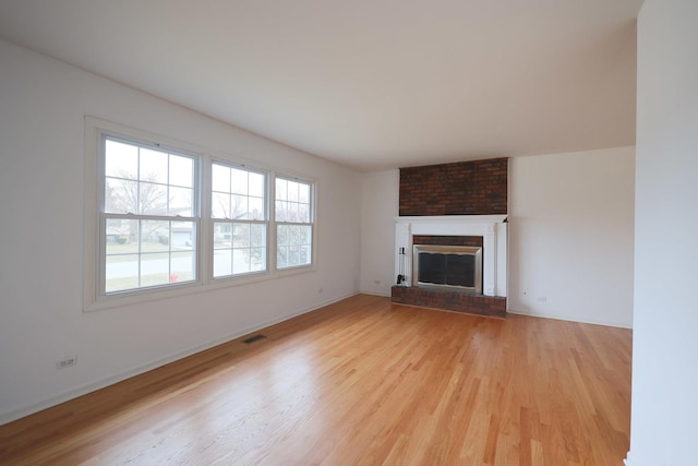 unfurnished living room with visible vents, light wood finished floors, plenty of natural light, and a brick fireplace