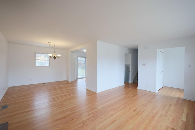 spare room with light wood-style floors, an inviting chandelier, visible vents, and stairway
