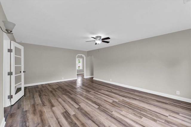 spare room with arched walkways, baseboards, a ceiling fan, and dark wood-style floors
