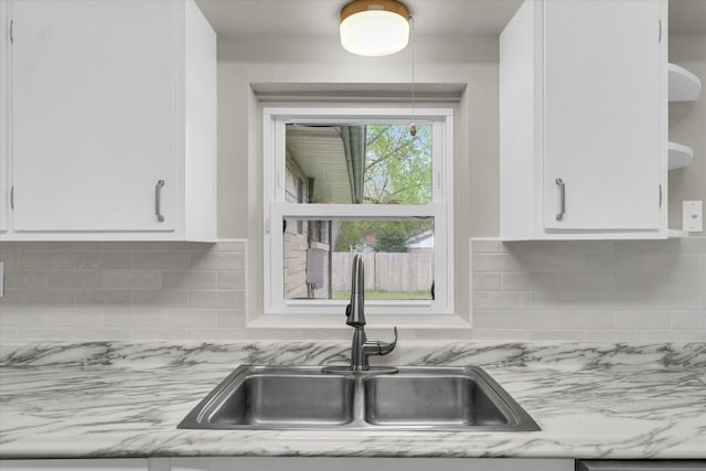 kitchen with open shelves, light stone counters, a sink, white cabinetry, and backsplash