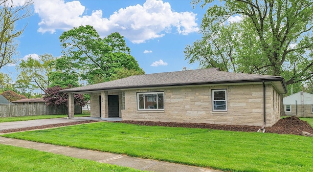 single story home featuring fence, a front yard, stone siding, a shingled roof, and concrete driveway