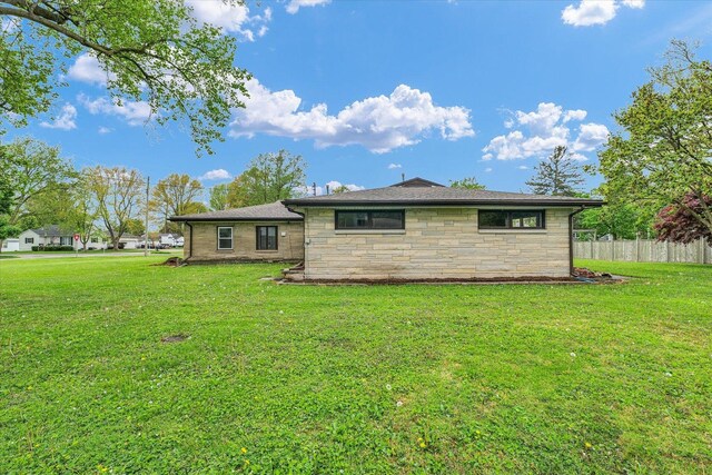 rear view of house featuring a lawn, fence, and stone siding