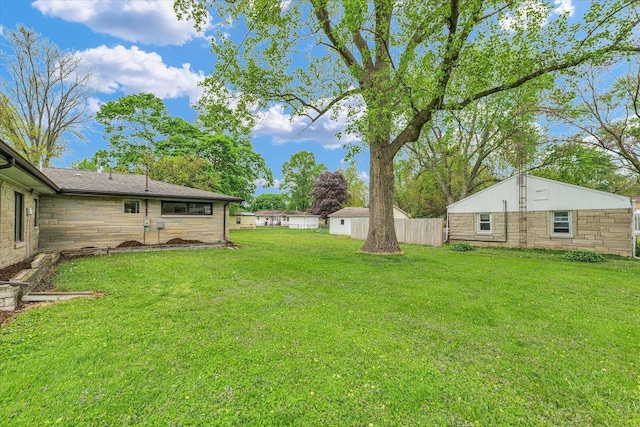 rear view of house featuring a lawn, fence, and stone siding